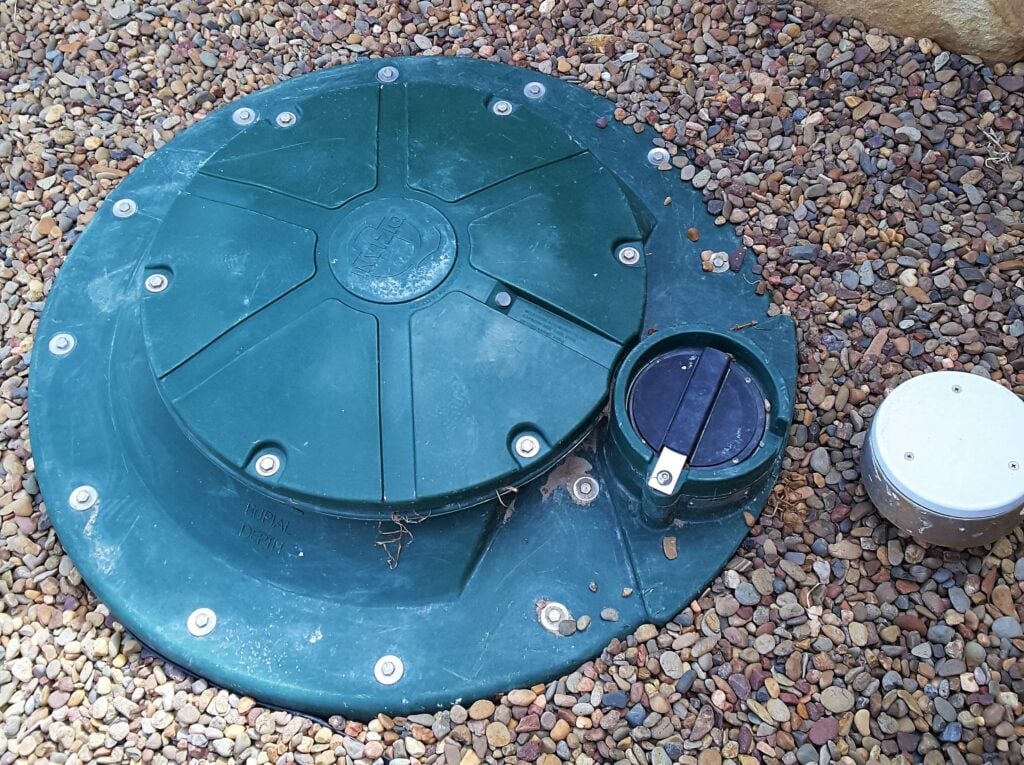 A circular, dark green plastic septic tank riser and lid assembly