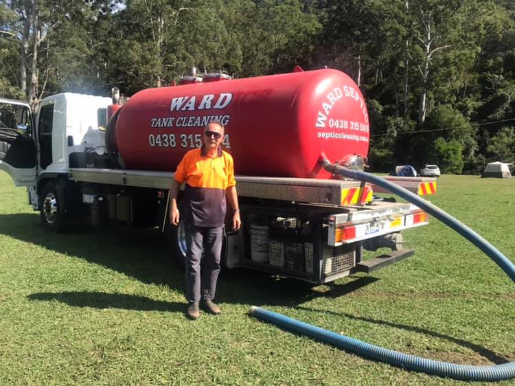 Ward Tank Cleaning service truck with a large red vacuum tank and a long blue hose on a grassy field.