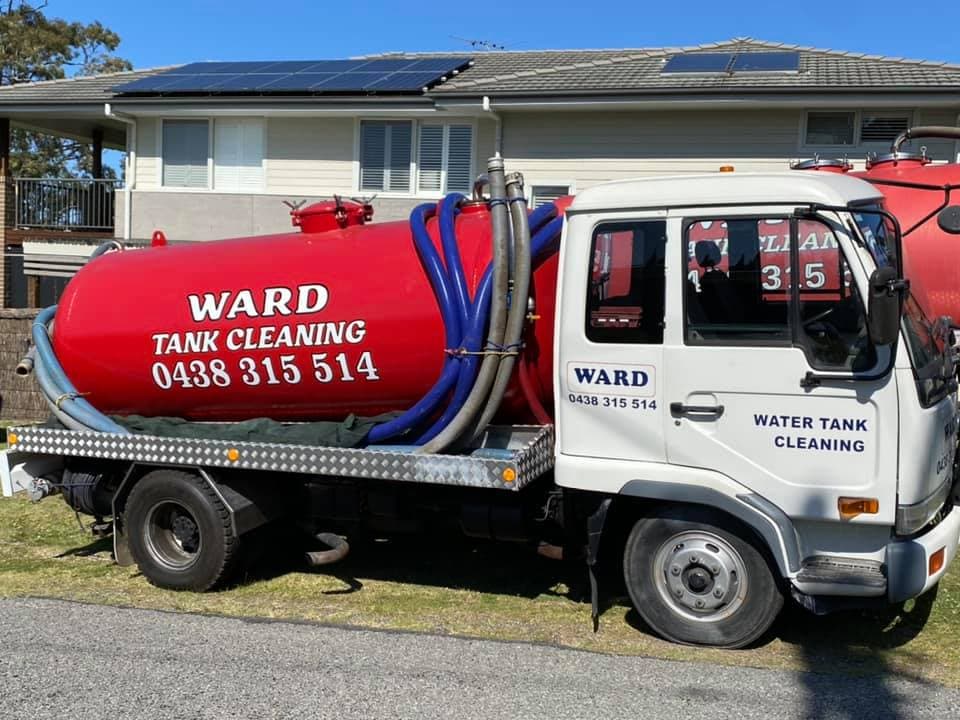 A side view of a white Nissan service truck with a large red vacuum tank labelled "WARD TANK CLEANING" and a phone number