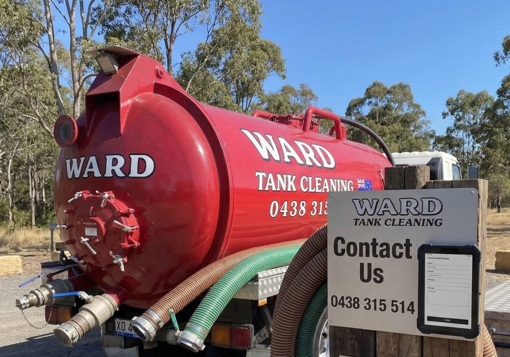 A red Ward Tank Cleaning truck parked outdoors next to a contact sign and hoses.