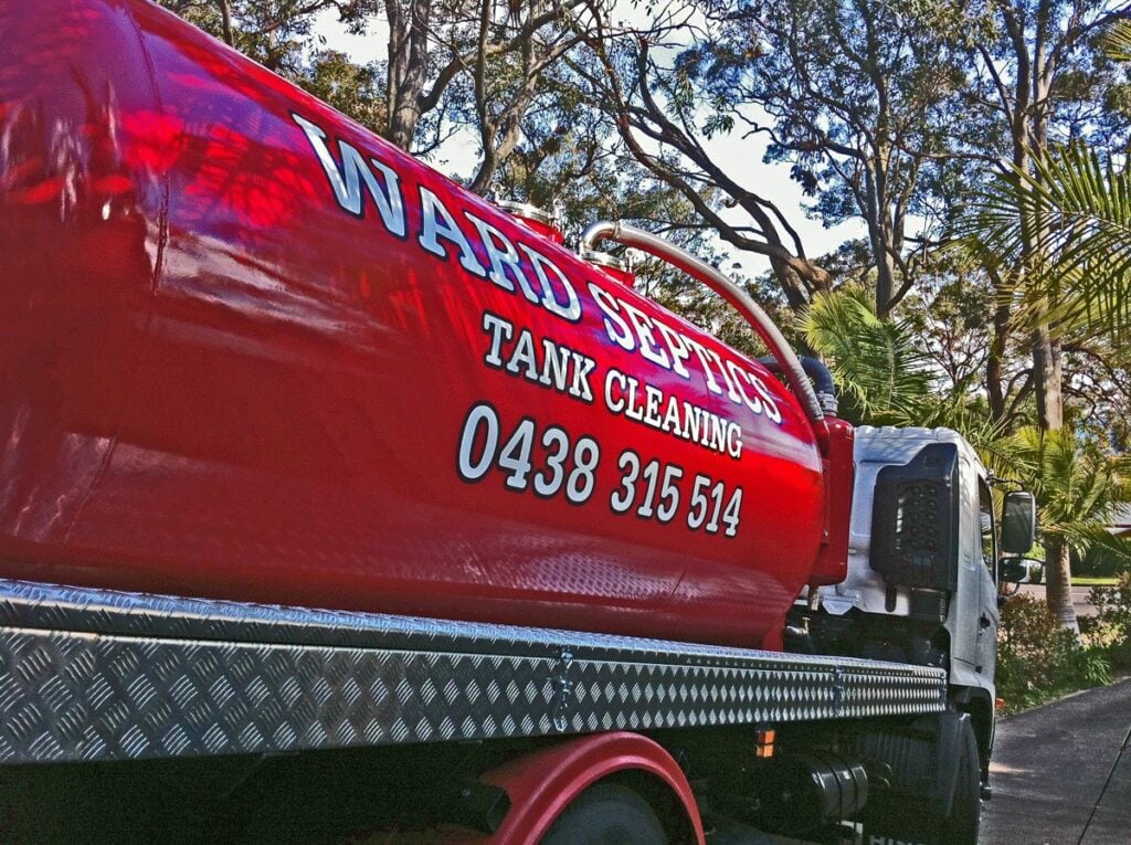A large red septic tank cleaning truck parked on a paved driveway