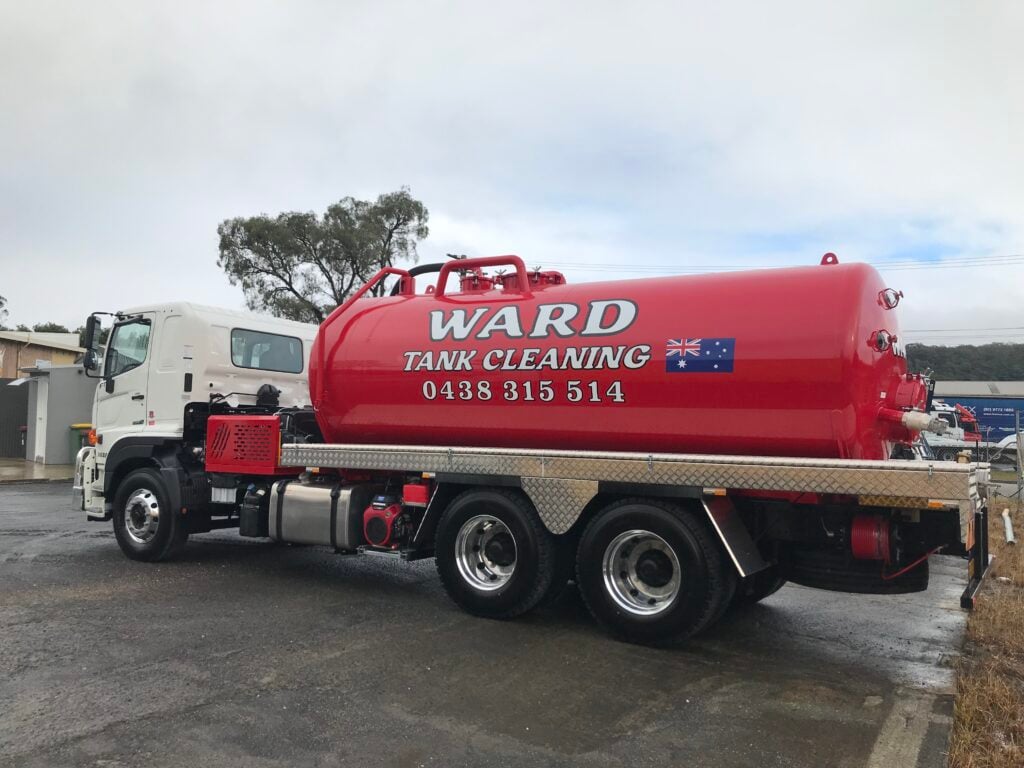 A white and red Ward Tank Cleaning truck parked on a paved surface under a cloudy sky.