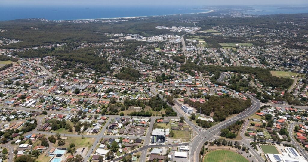 A sprawling coastal town or suburb with numerous residential houses, green spaces, and main roadways.