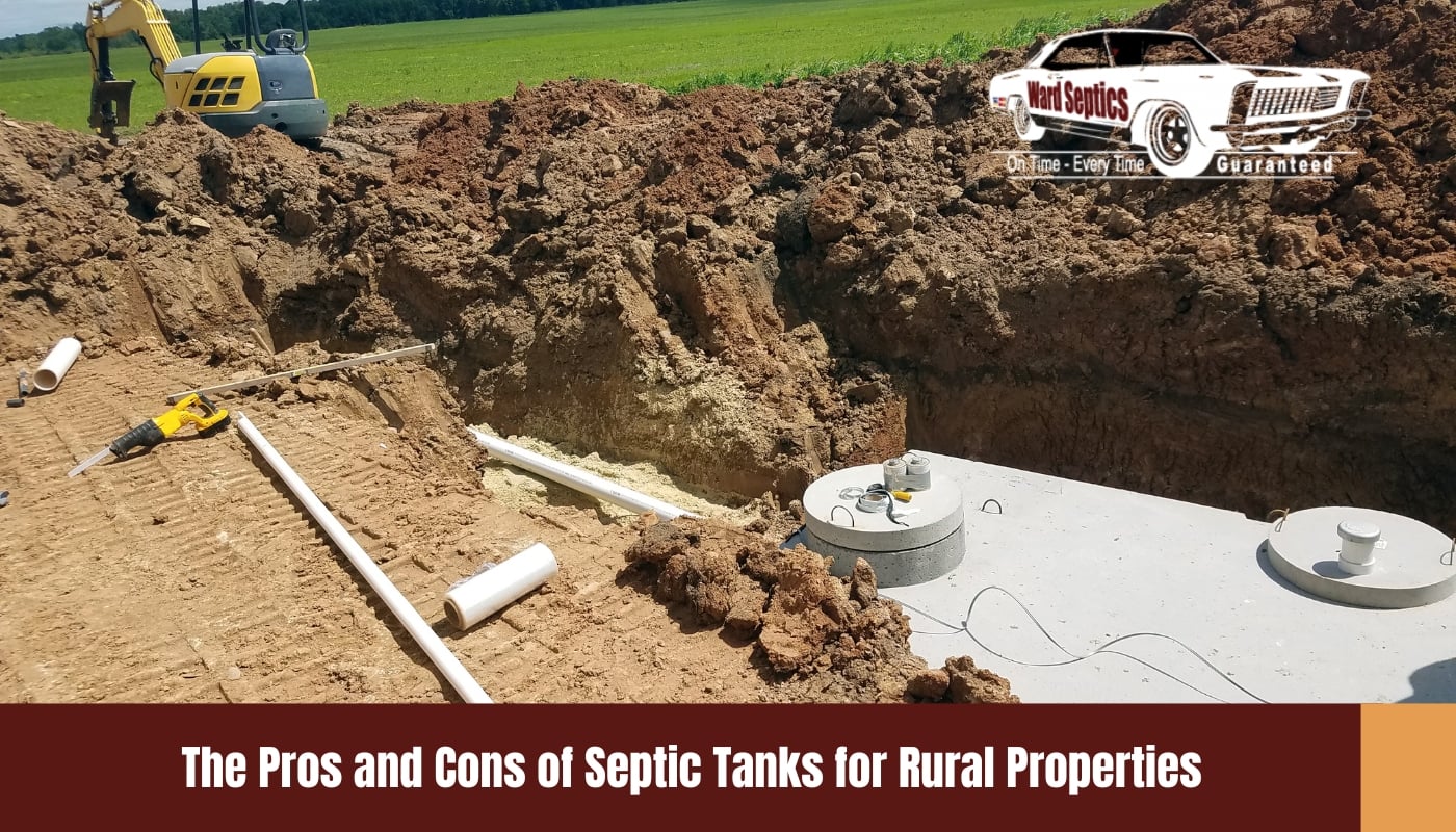 A large concrete septic tank being installed in a deep dirt excavation site with PVC pipes laid nearby.