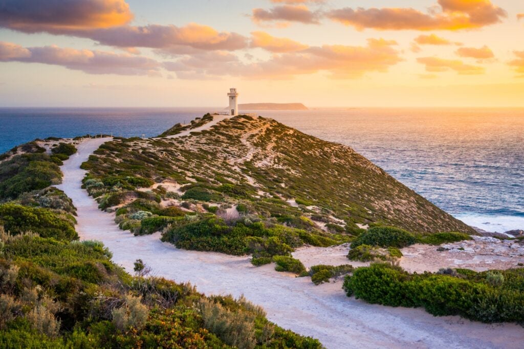 A white lighthouse stands atop a coastal hill at sunset
