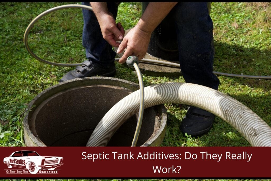 A small yellow line next to a large corrugated suction hose lowered into an open concrete septic tank manhole.
