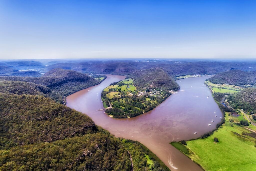 Aerial view of a wide river curving around a lush green peninsula surrounded by forested hills.