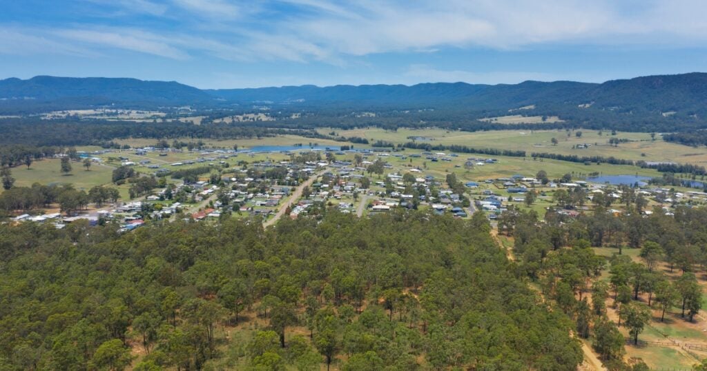 A small rural town nestled in a wide, grassy valley, bordered by dense forests in Millfield.