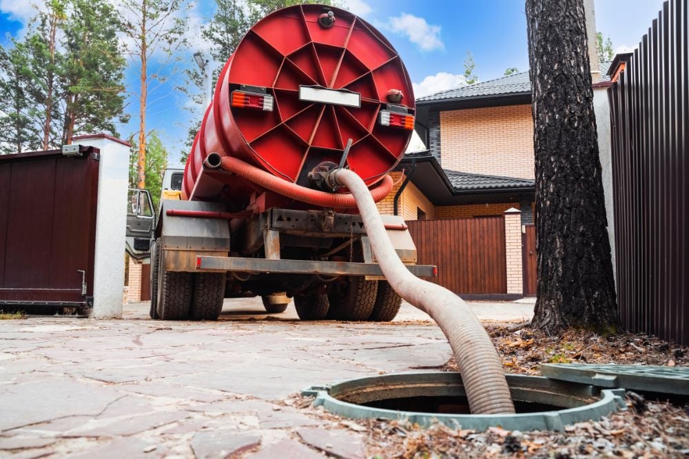 The rear of a red vacuum truck with a large tank parked in a stone driveway