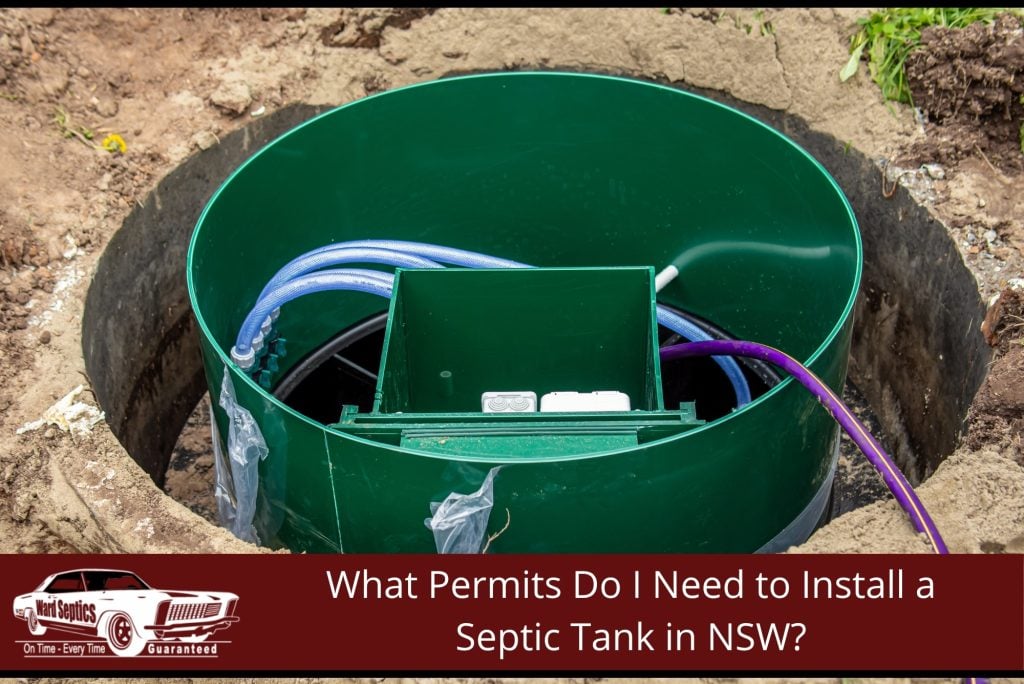 A large green cylindrical septic tank riser installed in a dirt pit, showing internal wiring, a plastic manifold box, and purple and blue plumbing lines.