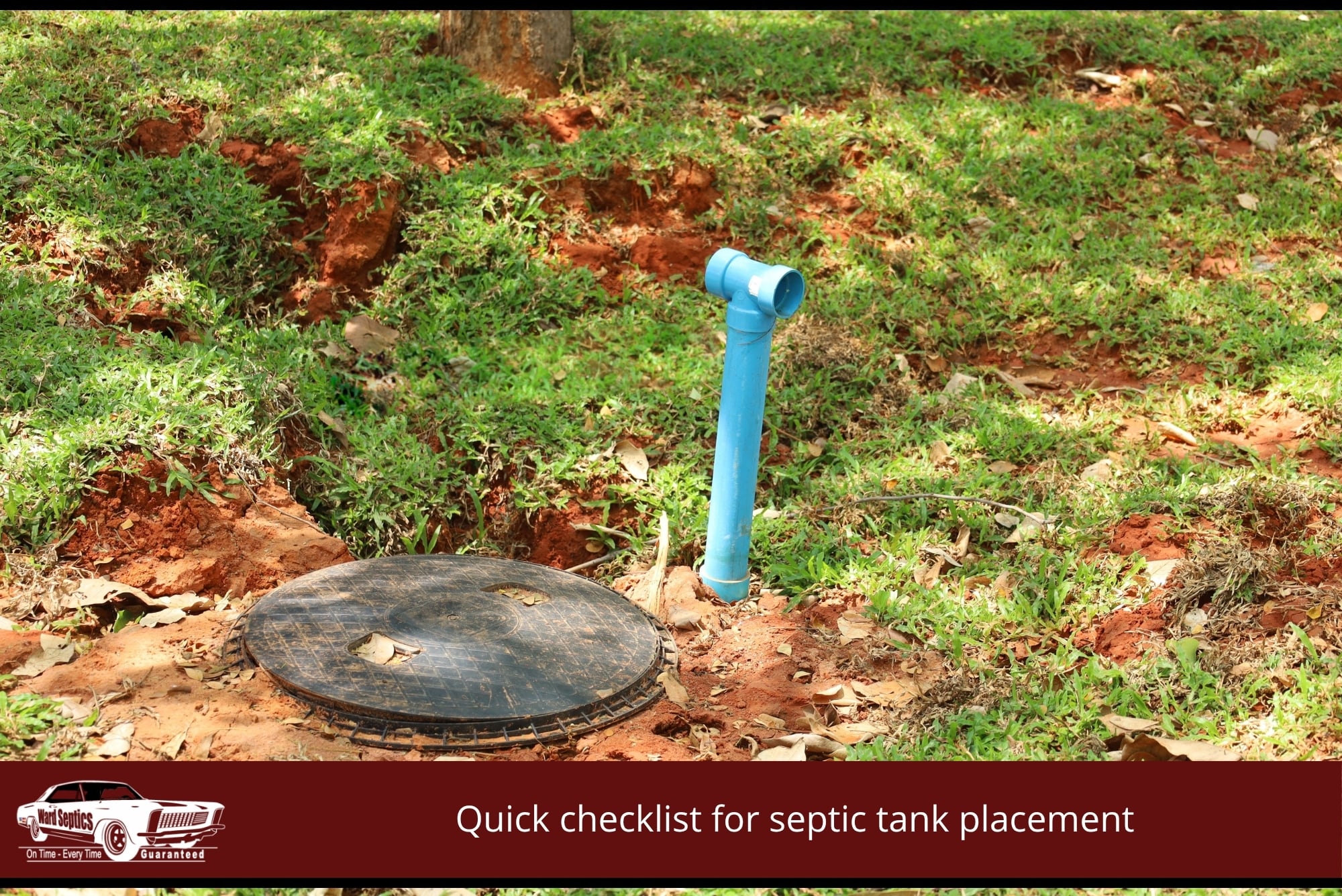 A black circular septic tank manhole cover and a blue PVC T-junction pipe installed in a grassy area with red soil.