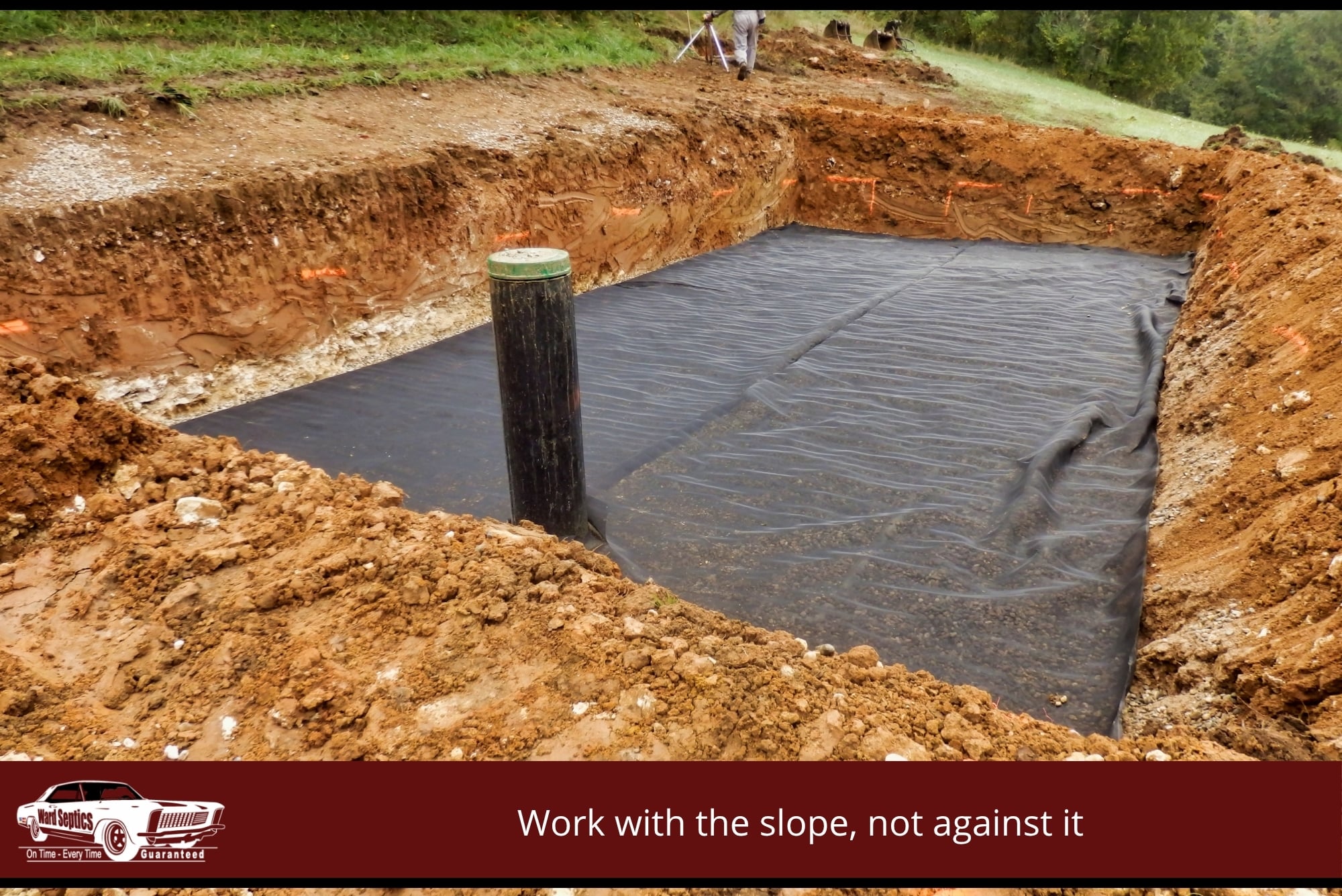 Large rectangular excavation for a septic drain field lined with black geotextile fabric and a vertical PVC riser pipe.