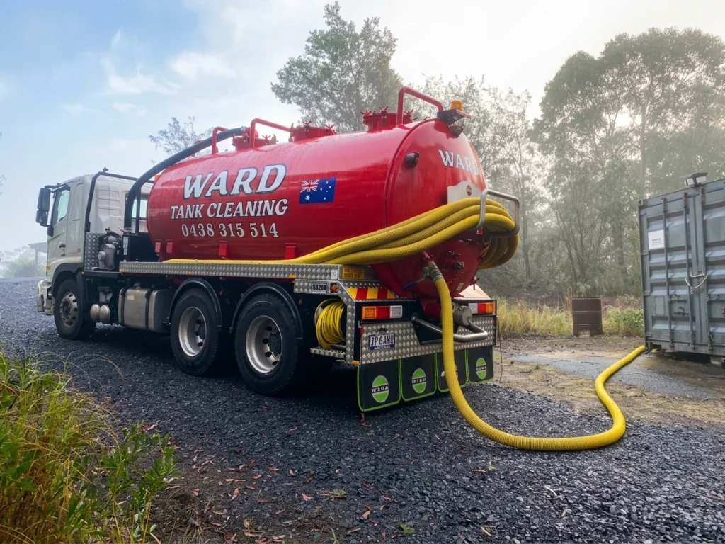 Red Ward Tank Cleaning truck servicing a container unit with a yellow hose attached.