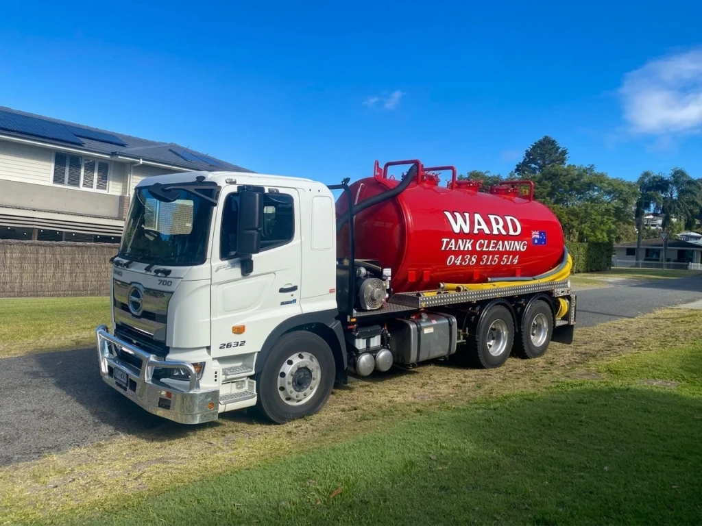 White Hino Ward Tank Cleaning truck parked outside a house on a sunny day.