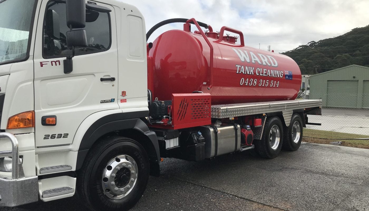 A front-angled view of a white Ward Tank Cleaning truck with a red vacuum tank, parked on a wet asphalt surface.